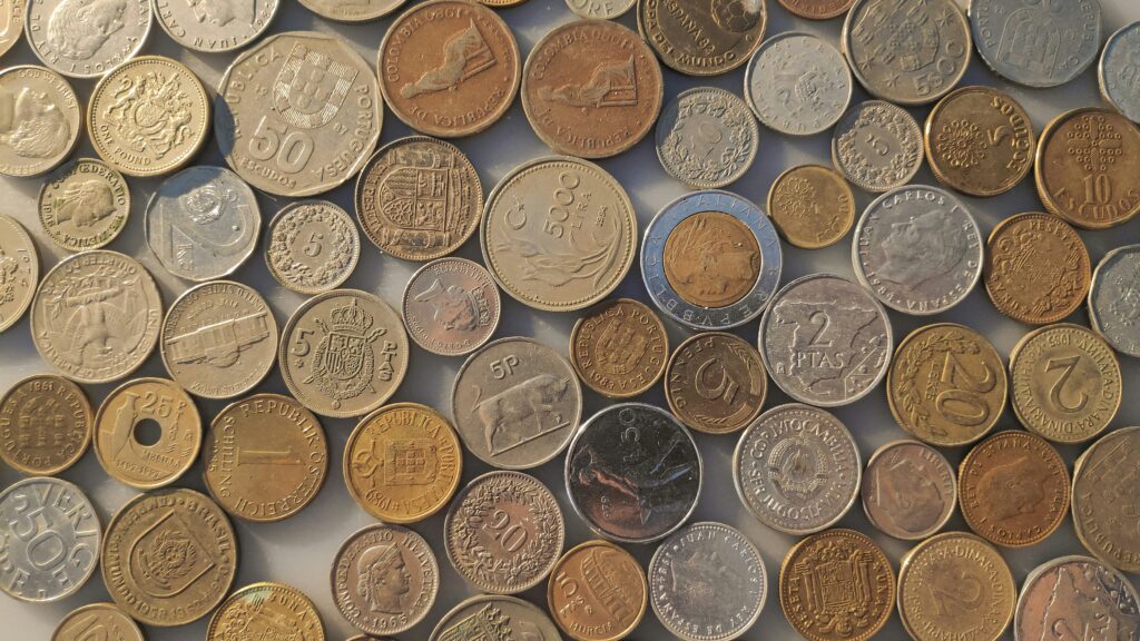 A collection of various coins from different countries, laid out on a flat surface. The coins vary in size, design, and color, showcasing a mix of metals like silver, bronze, and gold.